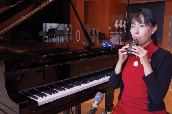 Faculty member sitting by a piano and blowing into a small instrument