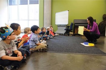 Teacher holding up a piece of paper to a group of young children sitting on the floor