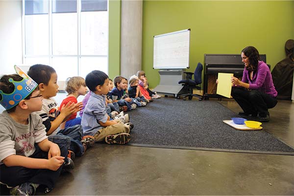 Teacher holding up a piece of paper to a group of young children sitting on the floor