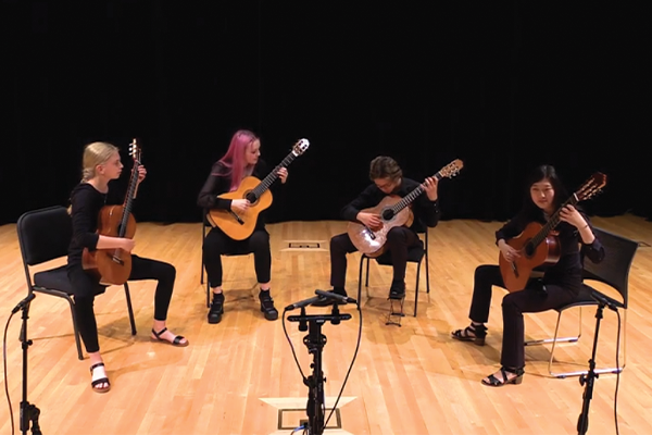 4 students playing guitar on a stage