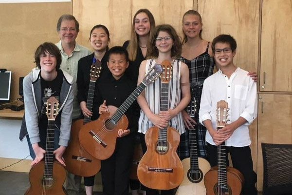 Group of students standing with their teacher. All are holding guitars
