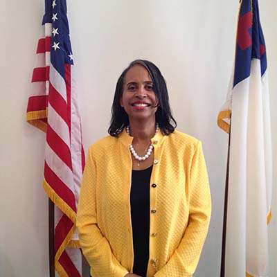 Dianne wearing a yellow shirt and standing in front of two flags