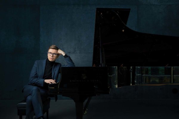 Person wearing a dark suit sitting at a piano