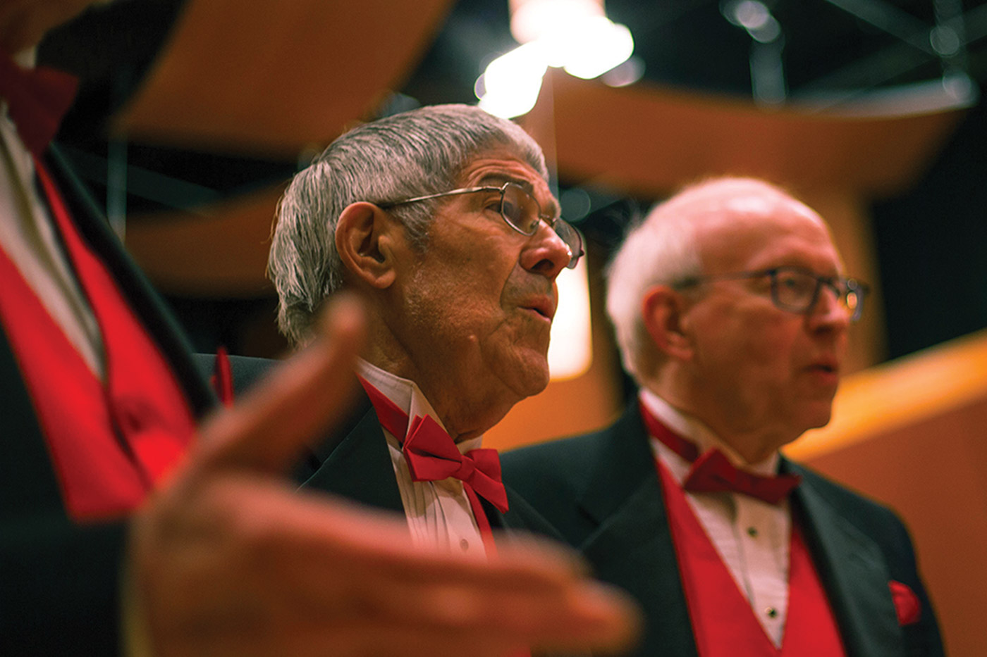 Three older adults wearing red bow ties and singing